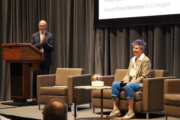 Carol Clark, APHL's COO, sits on a stage with a birthday cake