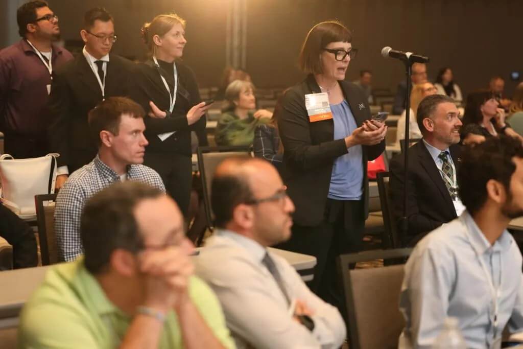 Conference attendees stand at a microphone to ask a speaker questions.