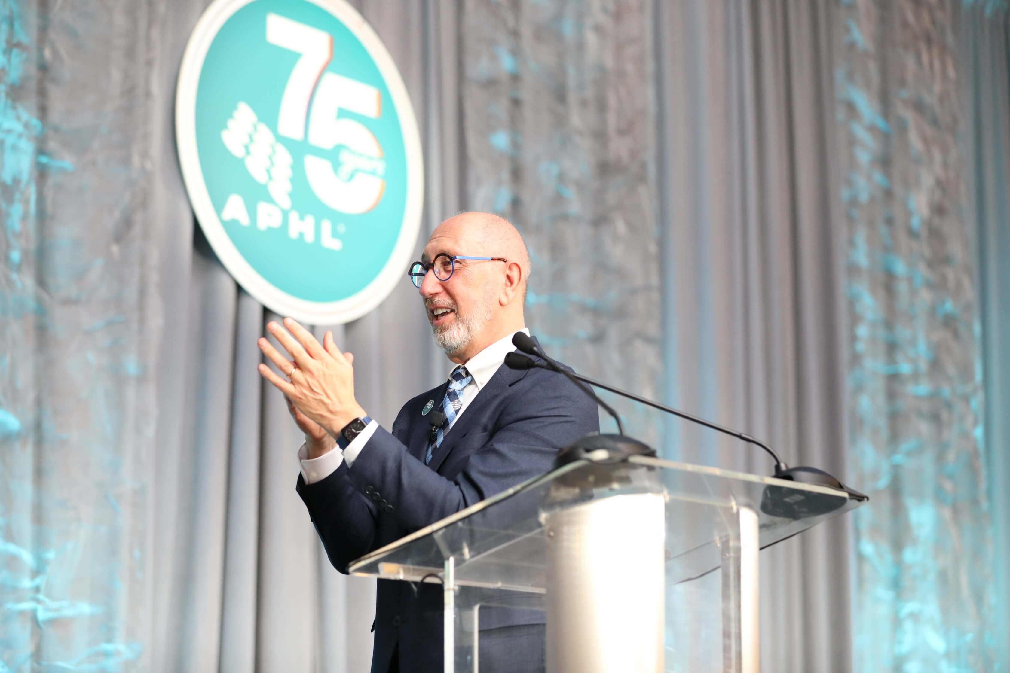 Scott Becker on stage at APHL2026 with APHL's 75th anniversary logo in the background