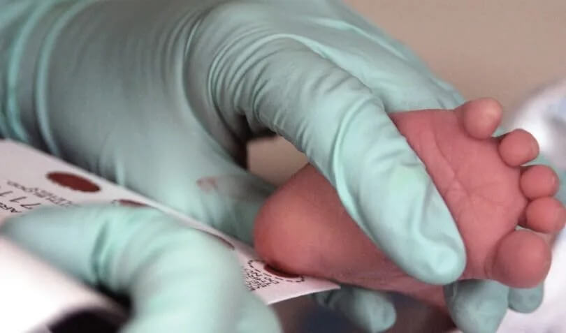 A gloved hand holding an infant's foot