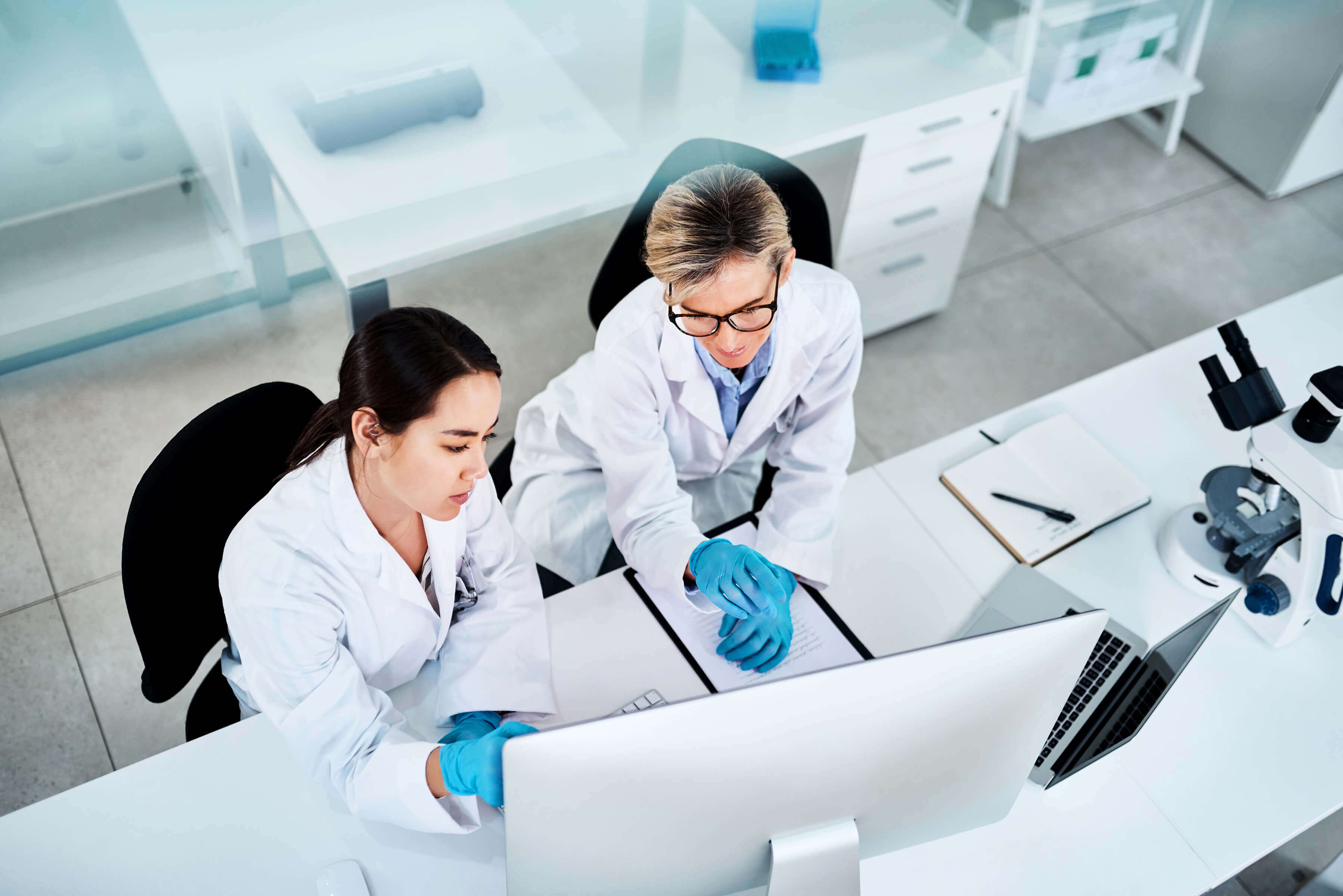 two female scientists sit at a lab bench looking at a computer screen