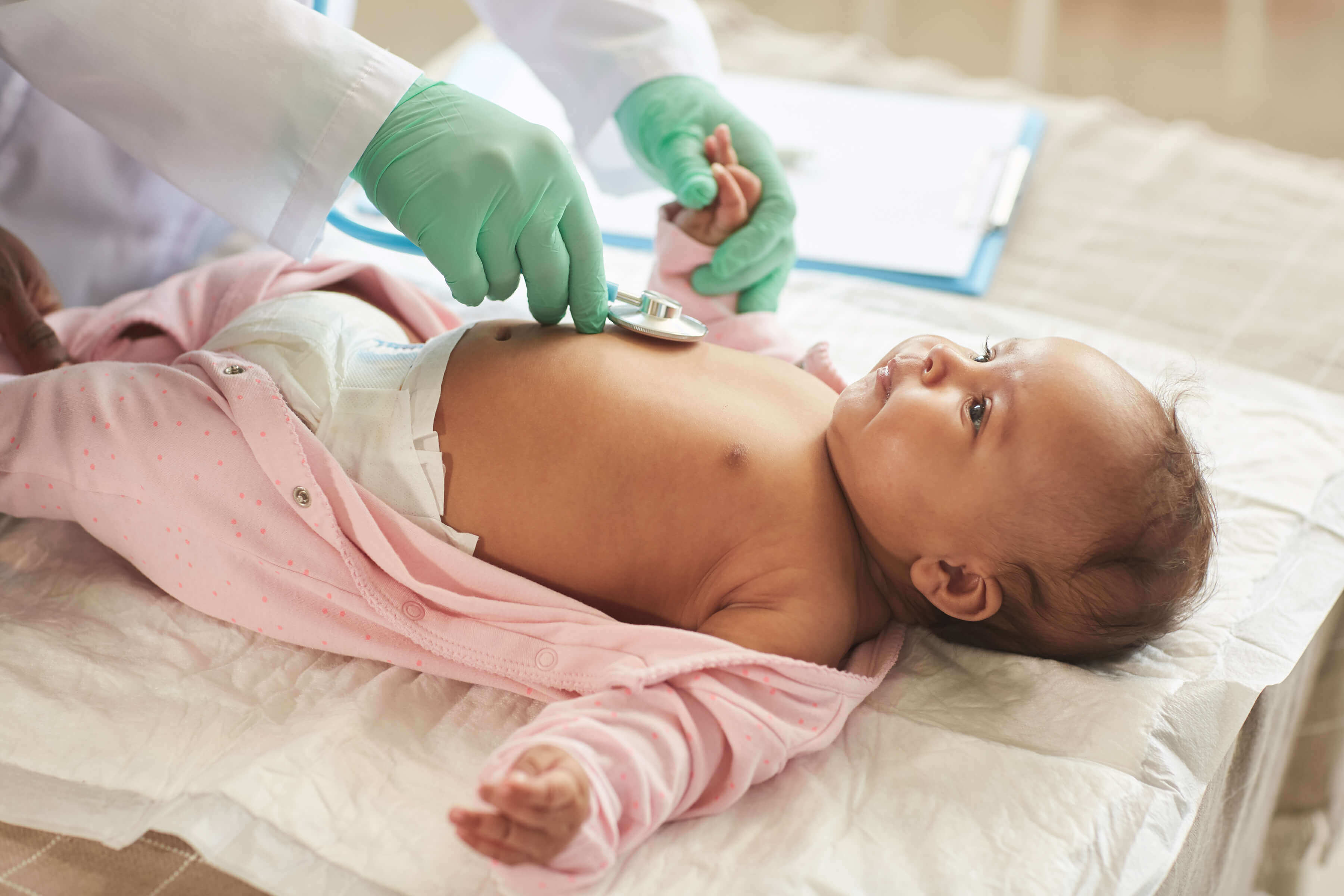 doctor wearing medical gloves holds a stethoscope to a newborn baby's chest