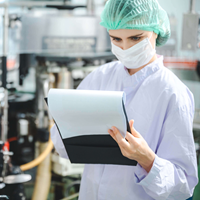 woman in a lab with hairnet and mask holding a clipboard