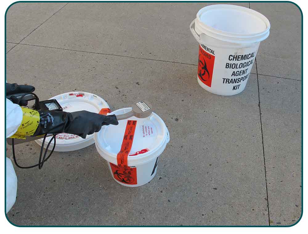 North Dakota Public Health Laboratory staff use a handheld radiation detector to scan over-pack packaging for radiation during a drill